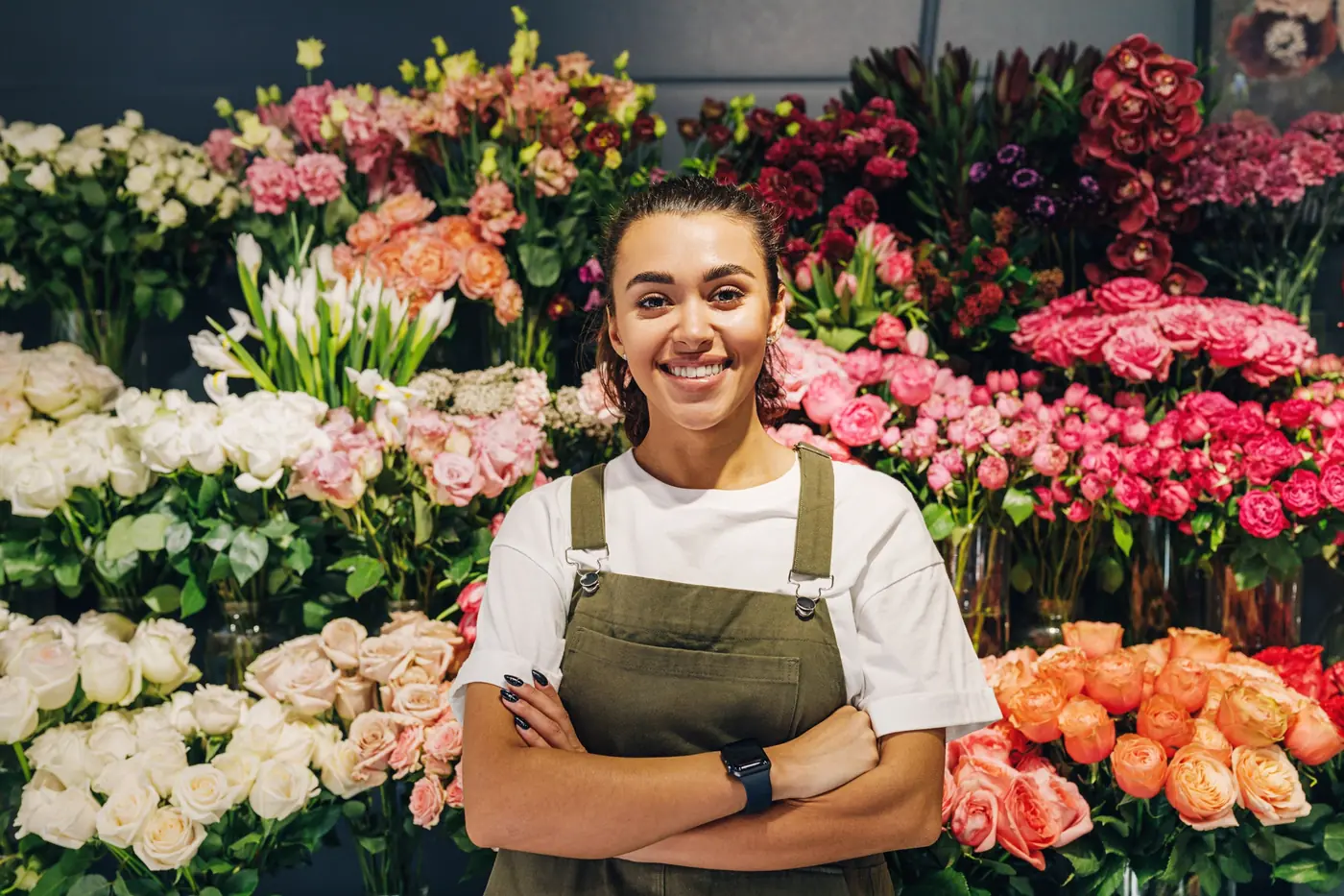 Fleuriste dans sa boutique devant un mur de roses, œillets et fleurs de saison